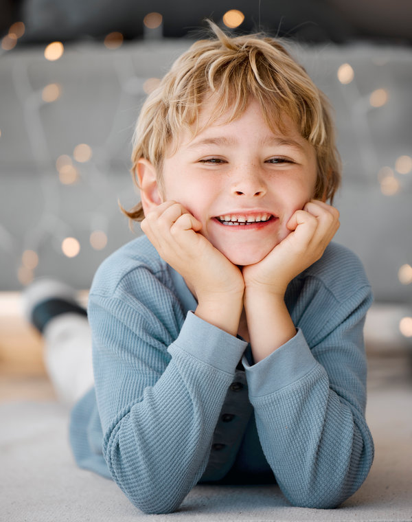 Portrait smile, boy and lying on floor in home for wellness, relax and alone time with bokeh lights. Face, young child and happy on carpet with healthy gums, clean mouth and dental care for teeth.